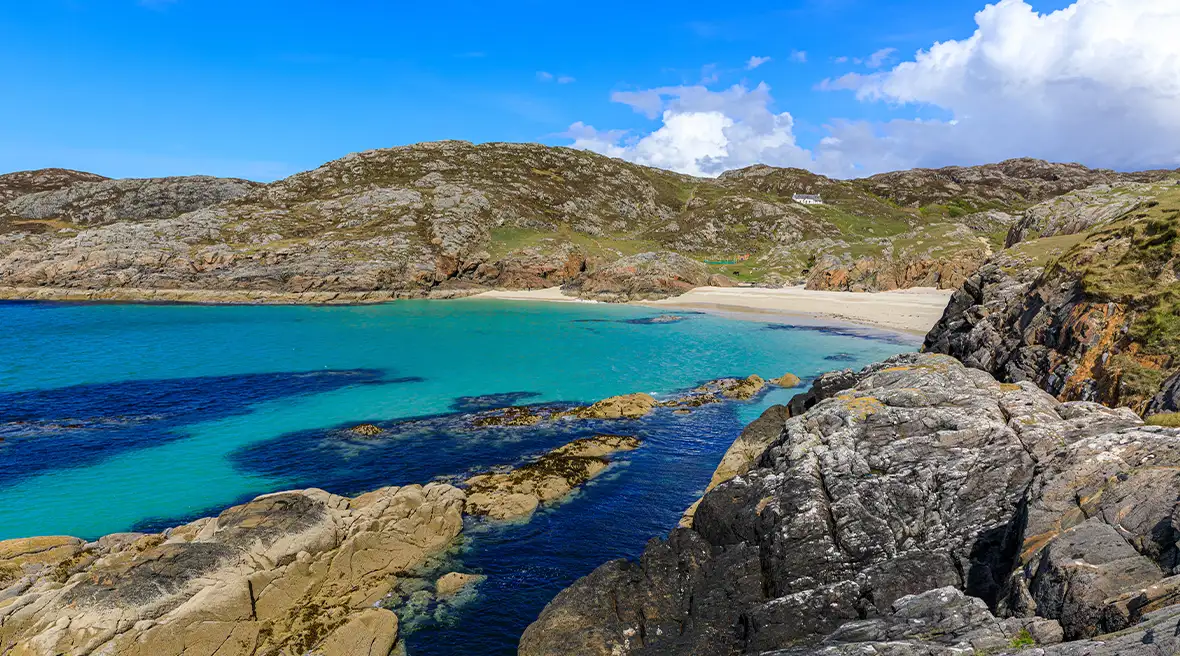 Klares, blaues Wasser und ein Sandstrand, umgeben von einer felsigen Küstenlandschaft